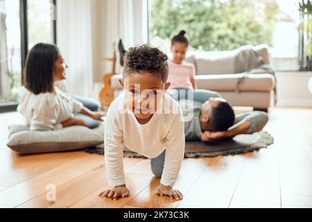 Vermisse mich mit diesen Kitzeln. Porträt eines entzückenden kleinen Jungen, der kriecht, während sich seine Familie im Hintergrund auf dem Loungeboden verklebt. Stockfoto