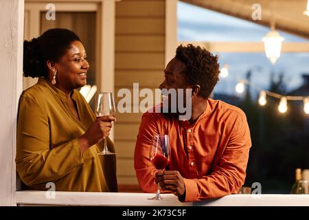 Porträt eines jungen afroamerikanischen Paares, das abends auf der Terrasse des Hauses Wein genießt Stockfoto