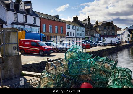 Eine Reihe von bunten Häusern und Geschäften mit Hummer-Töpfen und geparkten Autos am Kai am East Loch Tarbert. Argyll und Bute Stockfoto