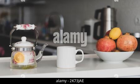 Weißer Becher-Mockup. Weißer leerer Becher-Mockup in einer modernen Küche mit heißem Tee und frischen Früchten wie Granatapfel-Zitrone. Cup-Mockup, dass Cup-Verkäufer Stockfoto