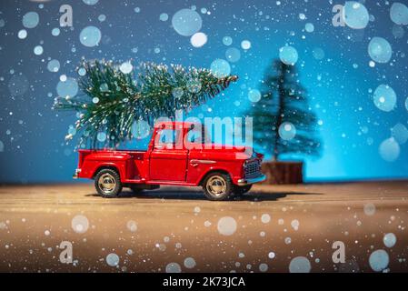 Ein Spielzeug roten Retro-Auto trägt einen Weihnachtsbaum an Weihnachten und Silvester auf einem blauen Hintergrund. Stockfoto