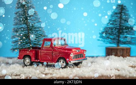 Ein Spielzeug roten Retro-Auto trägt einen Weihnachtsbaum an Weihnachten und Silvester auf einem blauen Hintergrund. Stockfoto