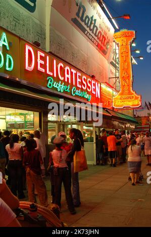 Eine Menschenmenge versammelt sich nachts vor den Neonlichtern des ursprünglichen Nathans Hot Dogs Fast-Food-Restaurants in Coney Island, Brooklyn, New York City Stockfoto