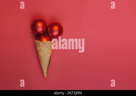 Alternative Eiscreme-Weihnachtskugeln in einem Waffelkegel auf rotem Hintergrund. Runde Spielzeuge mit Goldfaden. Weihnachtsfeier im Winter Konzept, Ansicht von oben festliche Komposition. Flach Liegend Stockfoto