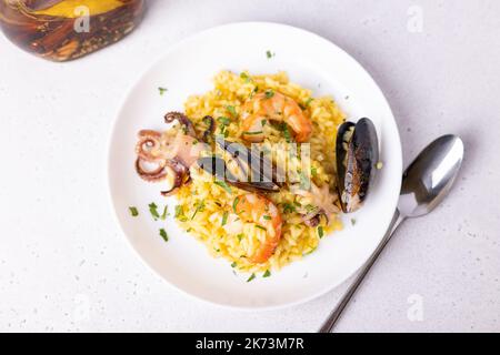 Risotto mit Meeresfrüchten mit Safran und Petersilie. Arborio-Reis mit Garnelen, Muscheln und Babykrake. Traditionelles italienisches Gericht. Nahaufnahme, selektiver Fokus Stockfoto