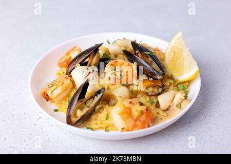 Risotto mit Meeresfrüchten mit Safran, Petersilie und Zitrone. Arborio-Reis mit Garnelen, Muscheln und Tintenfisch. Traditionelles italienisches Gericht. Nahaufnahme, selektiver Fokus Stockfoto