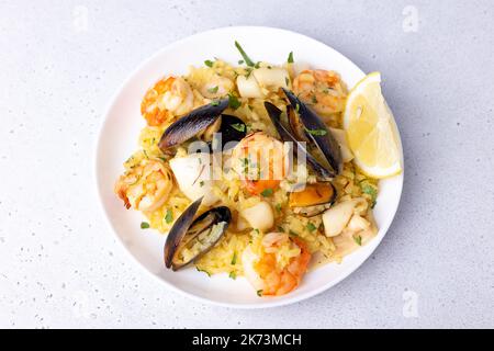 Risotto mit Meeresfrüchten mit Safran, Petersilie und Zitrone. Arborio-Reis mit Garnelen, Muscheln und Tintenfisch. Traditionelles italienisches Gericht. Nahaufnahme, selektiver Fokus Stockfoto