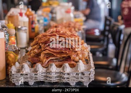 Stapel Speck auf dem Tresen im lokalen Diner während der Frühstückszubereitung. Absichtlich selektiver Fokus und Hintergrundunschärfe. Stockfoto