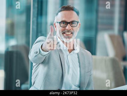 Verbreiten Sie Liebe überall Sie gehen. Ein reifer Geschäftsmann, der bei der Arbeit Daumen nach oben zeigt. Stockfoto