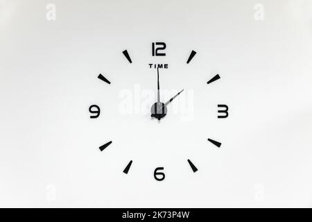 Minimalistische schwarze Zahlen und Pfeile einer Wanduhr auf weißem Hintergrund Stockfoto