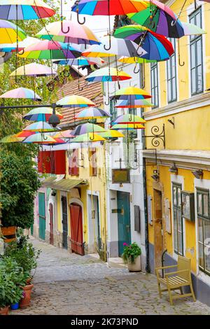 Bunte lustige Regenschirme hängen über der Straße in Szentendre mit Blumen Stockfoto