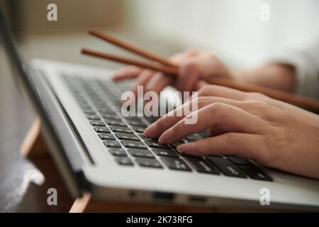Nahaufnahme der Geschäftsfrau, die beim Mittagessen Sushi isst, auf dem Laptop tippt Stockfoto