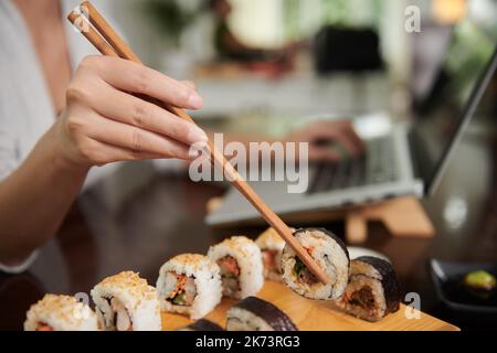 Hände einer jungen Frau, die beim Essen von Sushi zum Abendessen Essstäbchen verwendet Stockfoto