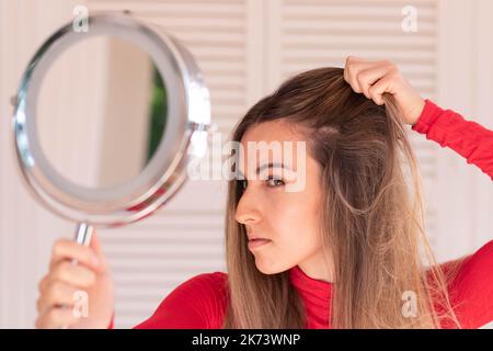 Junge schöne Frau, die auf den Spiegel schaut, der sich mit Alopezie beacause von Bleichen ungesunde Behandlungen beschäftigt Stockfoto