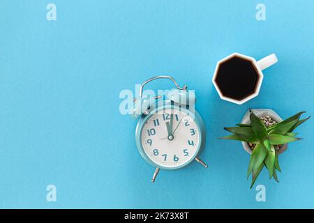 Wecker und eine Tasse Kaffee auf blauem Hintergrund, flach liegend. Stockfoto