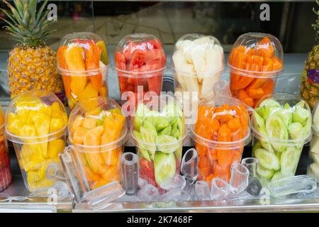 Exotische Fruchtstücke in Plastikbechern für Saftgetränke auf Eis am Marktstand. Gesunde Erfrischung auf der Straße Stockfoto