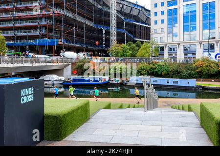 Grüne Stufen am Getreideplatz und Jogger auf dem Abfluss des Regents Canal, Bauarbeiten am gegenüberliegenden Ufer am King's Cross, London, Großbritannien Stockfoto