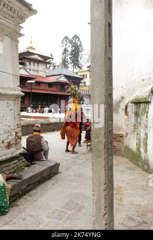 Ein Mann repräsentiert Shiva in menschlicher Form und zieht an die Stelle des Tempels. Er trägt einen Blumenkranz und den Körper, der in Orange gemalten ist, entsprechend der Statue, die Shiva darstellt, die sich am Eingang des Ortes befindet. Stockfoto