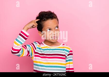 Foto von niedlichen liebenswert Schuljunge mit lockigen Haarschnitt tragen gestreiften langen Ärmeln suchen leeren Raum isoliert auf rosa Hintergrund Stockfoto