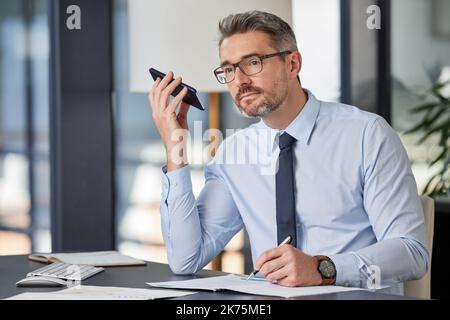 Ich habe Sie als Redner. Ein reifer Geschäftsmann, der an seinem Schreibtisch sitzt und in einem modernen Büro auf einem Mobiltelefon spricht. Stockfoto
