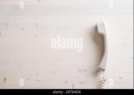 Einfaches weißes Festnetz-Telefon auf schlichtem Holzhintergrund mit viel Platz zum Kopieren auf der linken Seite eines Bildes. Stockfoto