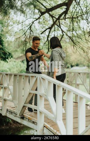 Erstaunliches Paar, das sich die Hände schüttelte und lachte, während es auf der weißen Brücke im Park stand Stockfoto