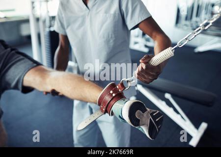 Nahaufnahme des Patienten, der sein Bein auf Sportgeräten trainiert, zusammen mit einer Krankenschwester, die ihn während der Übungen im Fitnessstudio unterstützt Stockfoto