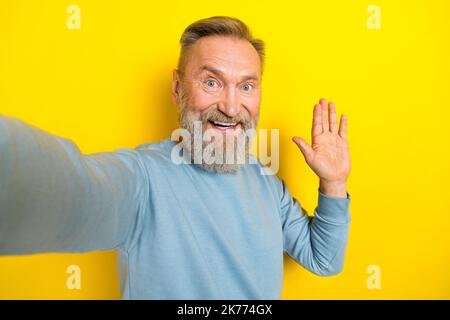 Foto von attraktiven freundlich pensionierten Kerl tragen blauen Pullover tacking Selfie winkende Arm Palm isoliert gelben Hintergrund Stockfoto