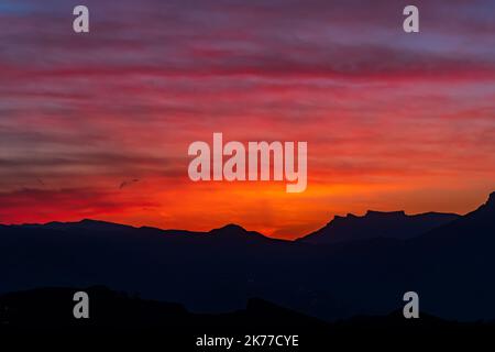 Natürlicher Hintergrund - heller, scharlachfarbener Sonnenuntergang über den Silhouetten von Berggipfeln Stockfoto