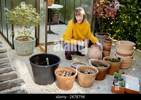 Frau pflanzt Blumen in Krügen im Garten Stockfoto