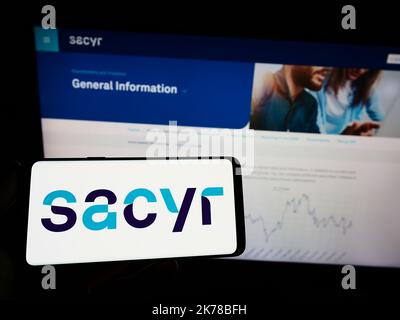 Person mit Mobiltelefon und Logo des spanischen Infrastrukturunternehmens Sacyr SA auf dem Bildschirm vor der Business-Webseite. Konzentrieren Sie sich auf die Telefonanzeige. Stockfoto