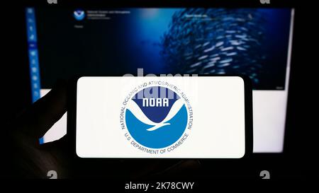 Person mit Telefon und Logo der National Oceanic and Atmospheric Administration (NOAA) auf dem Bildschirm vor der Website. Konzentrieren Sie sich auf die Telefonanzeige. Stockfoto