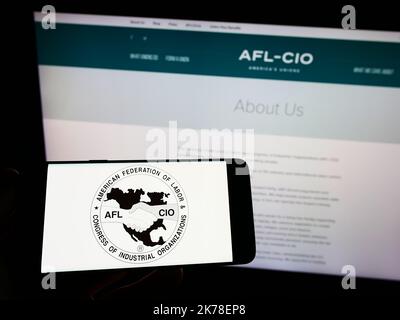 Person, die das Smartphone mit dem Logo des US-Gewerkschaftsbundes AFL-CIO auf dem Bildschirm vor der Website hält. Konzentrieren Sie sich auf die Telefonanzeige. Stockfoto