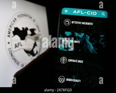 Person, die Mobiltelefon mit der Webseite des amerikanischen Gewerkschaftsbundes AFL-CIO auf dem Bildschirm vor dem Logo hält. Konzentrieren Sie sich auf die Mitte des Telefondisplays. Stockfoto