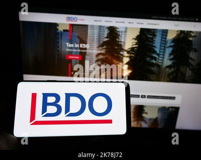 Person, die Mobiltelefon mit dem Logo des Buchhaltungs-Netzwerks BDO Global auf dem Bildschirm vor der Webseite des Unternehmens hält. Konzentrieren Sie sich auf die Telefonanzeige. Stockfoto