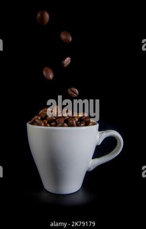 Weiße Tasse mit Kaffeebohnen auf schwarzem Hintergrund Stockfoto