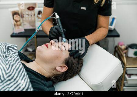 Ein Gesundheitsdienstleister, der einem Patienten eine nicht-invasive Gesichtsbehandlung zur Reinigung, Extraktion, Peeling und Hydratation gibt Stockfoto