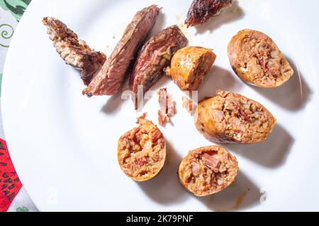 Gebratene und in Scheiben geschnittene Wurst auf einem weißen Gericht mit kleinen Fleischstücken neben dem Würstchengeschmack ist Pastrami. Stockfoto