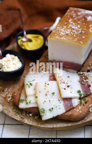 Frischer Schmalz mit Fleischschicht auf einem Holzbrett mit Gewürzen, Senf und Meerrettich. Leckerer Snack. Speck. Stockfoto