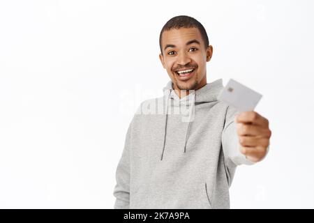 Porträt des glücklichen jungen Mannes erhält seine Bankkarte, zeigt Kreditkarte und lächelt, stehend auf weißem Hintergrund Stockfoto