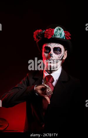 Junger Erwachsener mit Totenkopf-Make-up, der Daumen nach unten gibt, zeigt Missbilligung und Abneigung auf dem Schild, das Santa muerte traditionelles Kostüm trägt. Frau tut negative Geste am Tag der Toten. Stockfoto