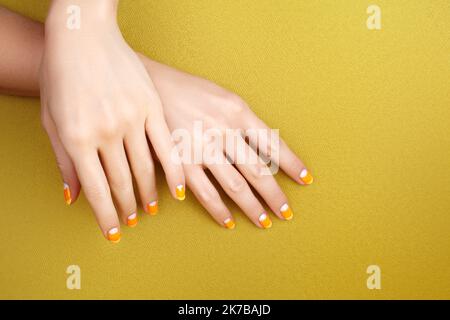 Schöne weibliche Hände mit leuchtend orange Maniküre wie Candy Corn. Gepflegte Nägel mit gelbem Gelpolitur. Halloween-Style Stockfoto