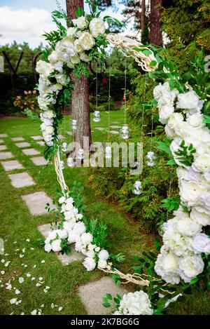 Hochzeitszeremonie. Sehr schöner und stilvoller Hochzeitbogen, geschmückt mit verschiedenen frischen Blumen, im Garten stehend. Hochzeitstag. Frische Blumen de Stockfoto