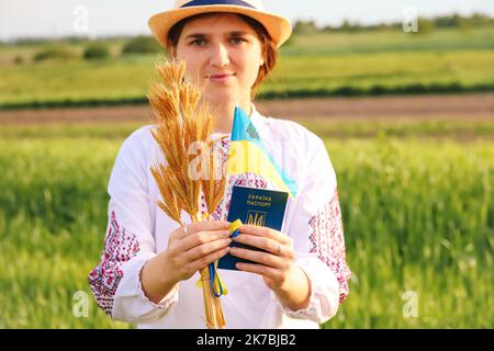 Unschärfe junge ukrainische Frau Porträt. Bouquet von reifen goldenen Dornen aus Weizen auf der Wiese Natur Hintergrund gebunden. Flagge Ukraine wird angezeigt. Lächelnd Stockfoto