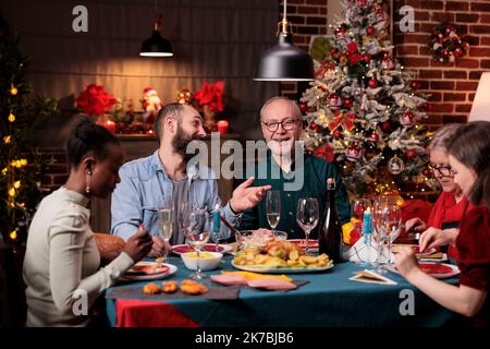 Familie feiert weihnachten zusammen, isst traditionelle Mahlzeit, genießt Gerichte am festlichen Esstisch. Weihnachtsfeier an einem wunderschön dekorierten Ort mit warmem Kerzenlicht Stockfoto