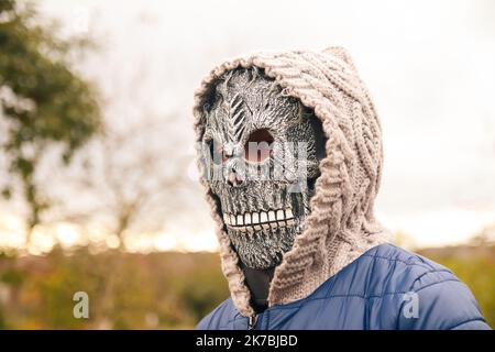 Unschärfe Halloween Menschen Porträt. Person in Sensenmann Maske auf Natur Herbst Hintergrund stehen. Halloween-Horror. Schädelgeist. Grimmiger Schnitter Stockfoto