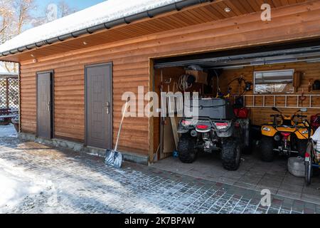 Fassadenblick, offene Tür, ATV-Hausgarage mit Quad-Bikes Offroad-Fahrzeug, das an sonnigen, schneebedeckten, kalten Wintertagen geparkt ist. ATV Abenteuer Extremsport. Haus organisiert Stockfoto