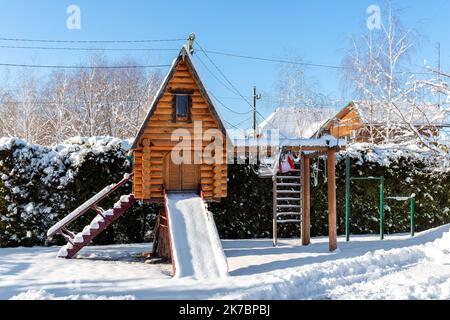 Kleines Holzblockspielhaus Teehaus Hütte schneebedeckte Treppen Leiter Holzrutsche Kinderspielplatz im Park oder Hof. Weiß schneebedeckte Lodge blau Stockfoto