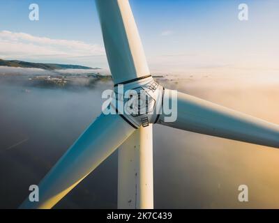 Nahaufnahme der Propeller einer Windenergieanlage während eines nebligen Morgens und Sonnenaufgangs. Grüne Energie. Windturbine bei Morgennebel Stockfoto