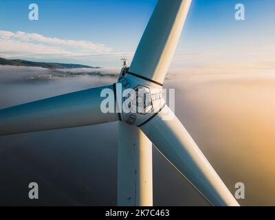 Nahaufnahme der Propeller einer Windenergieanlage während eines nebligen Morgens und Sonnenaufgangs. Grüne Energie. Windturbine bei Morgennebel Stockfoto